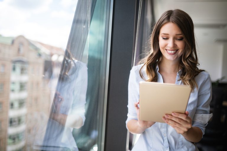 Happy woman manager holding tablet and standing in modern office