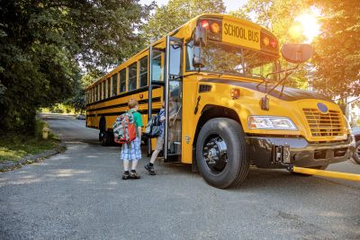 A young boy getting onto a school bus in sunshine