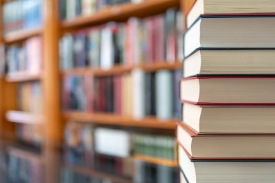 Many books stacked with blurred background of bookstore full of books. Photo with copyspace.